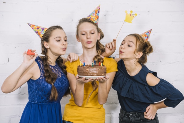 three teenage female friends blowing candles birthday cake